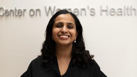 smiling woman standing in front of sign that reads "Center on Women's Health"