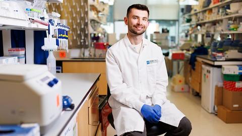 Man in lab coat sitting on stool and smiling