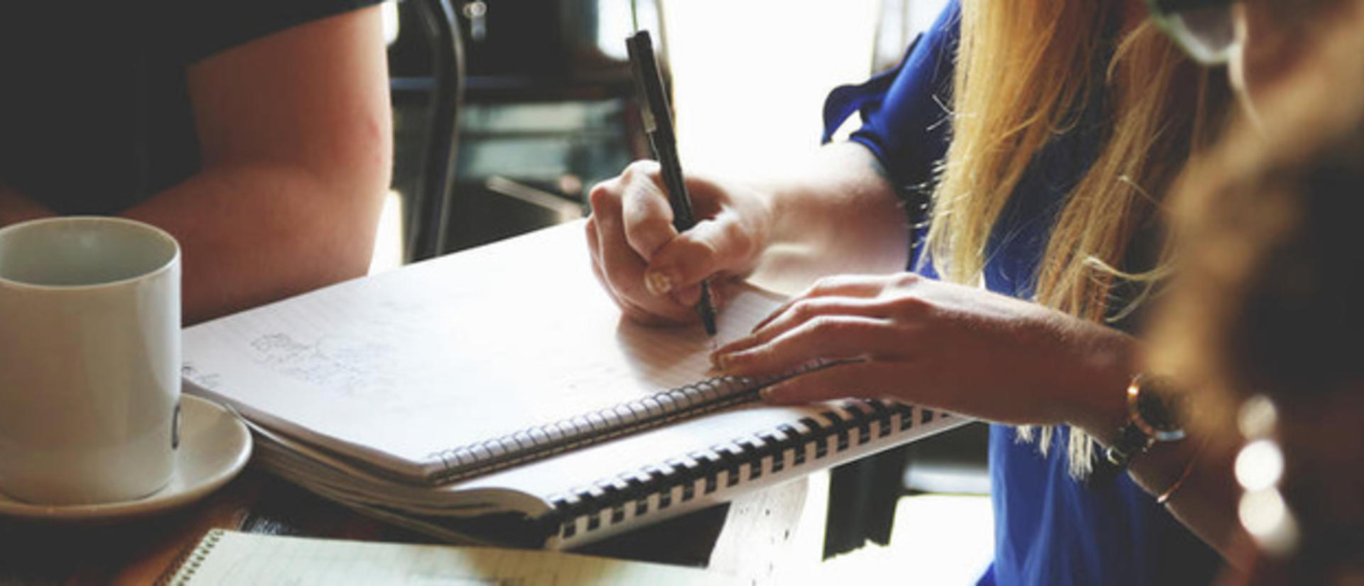 Person writing in a notebook with a cup of coffee